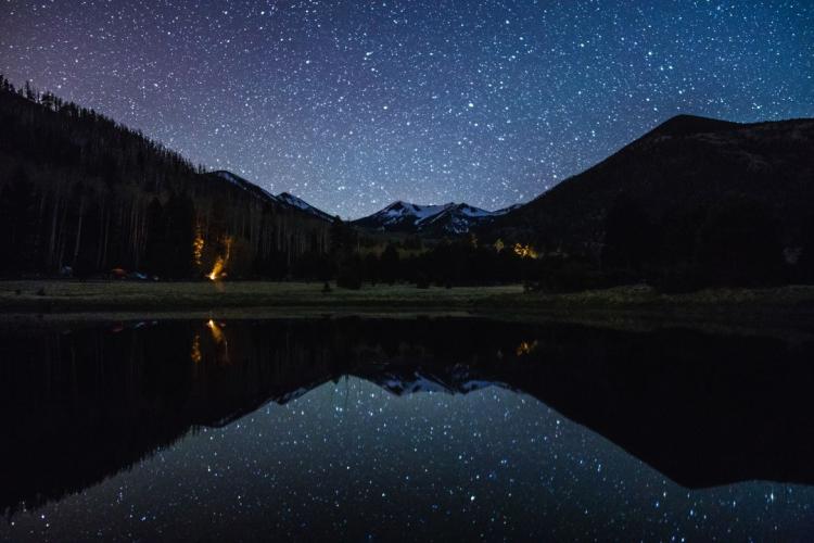 Stars reflect off of a lake surrounded by pine trees and mountains at Lockett Meadow. Photo Credit: @deborahsoltesz