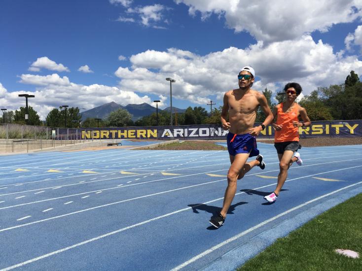 Two people running on the outdoor track at Northern Arizona University. Mountains are in the distance