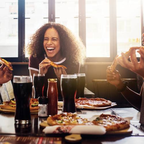 Friends laughing and eating pizza at a restaurant